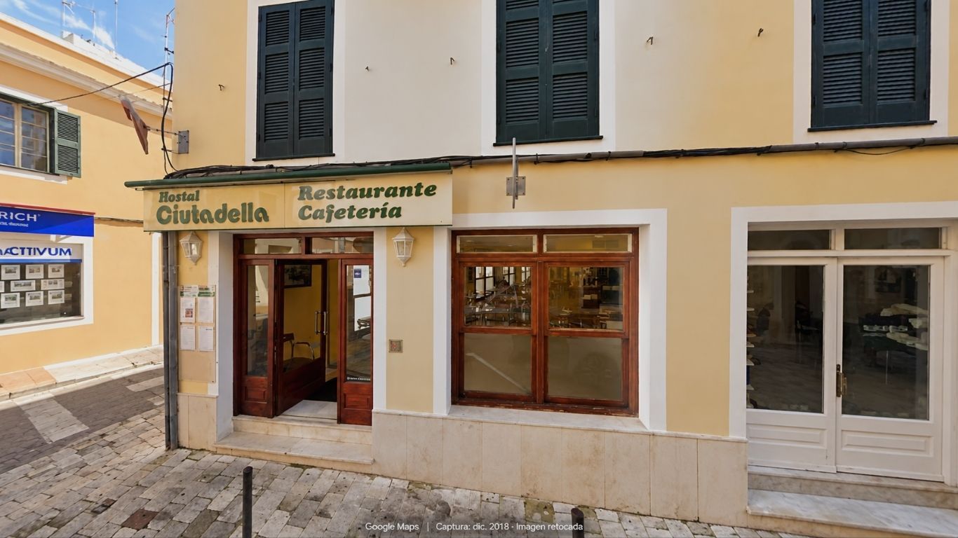 Façade of Sagitario Hostal Ciutadella with green shutters and a wooden entrance, in an edited image based on a 2018 capture